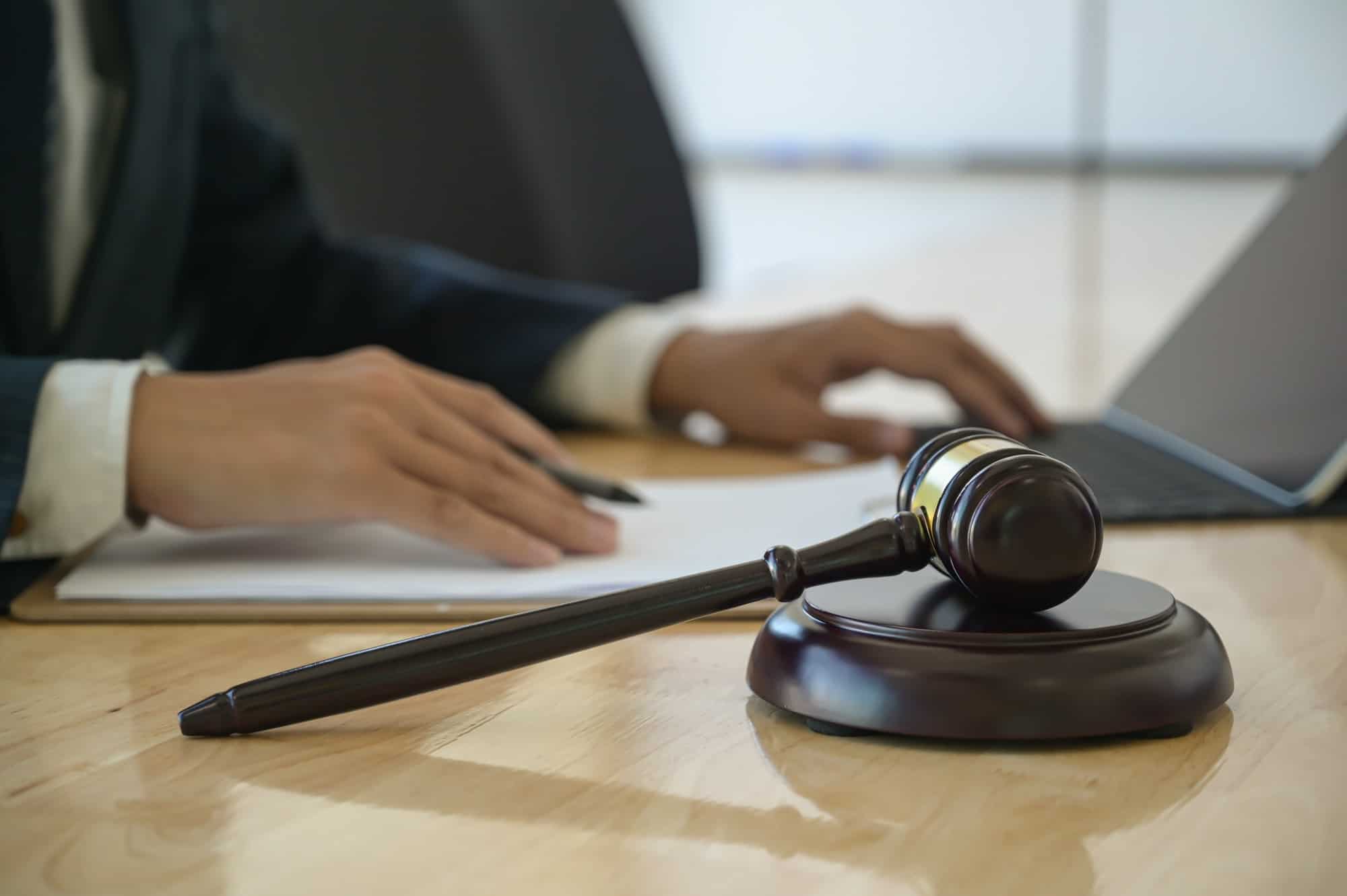 Concept of justice, Hammer placed on work desk with lawyer uses a laptop sitting behind. Concept of justice, Hammer placed on work desk with lawyer uses a laptop sitting behind.